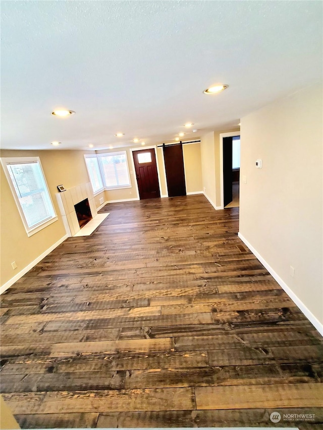 unfurnished living room with a barn door, dark hardwood / wood-style floors, and a tiled fireplace