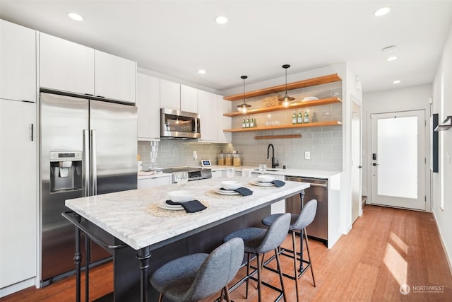 kitchen with appliances with stainless steel finishes, a breakfast bar, pendant lighting, light hardwood / wood-style flooring, and white cabinets