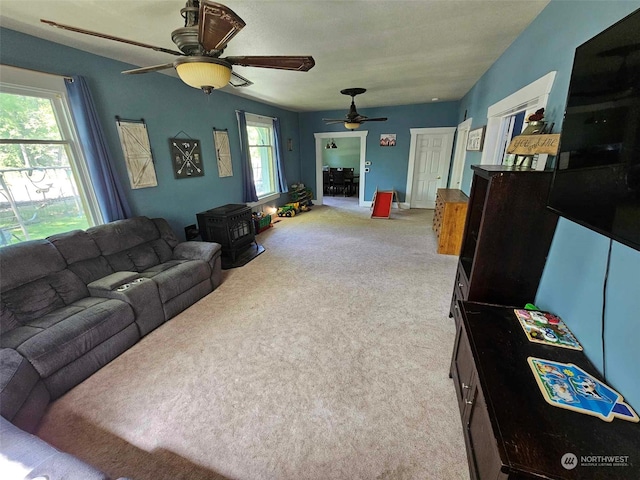 carpeted living room with a ceiling fan and a wood stove