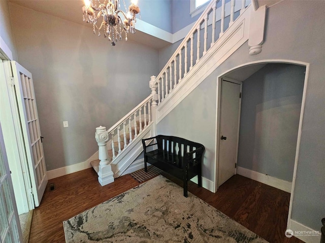 foyer entrance featuring wood finished floors, arched walkways, baseboards, a towering ceiling, and stairs