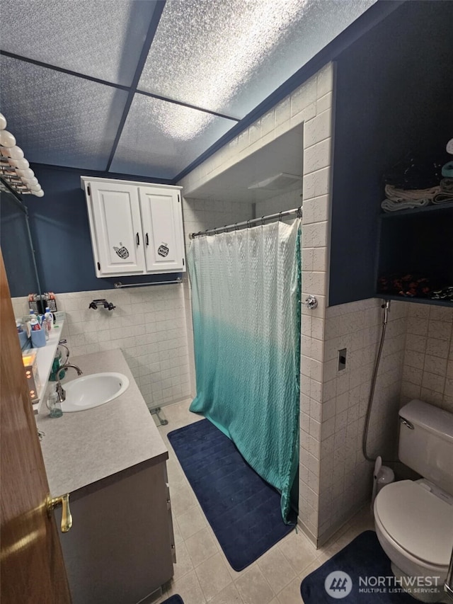 full bathroom featuring a shower with shower curtain, tile walls, wainscoting, and vanity