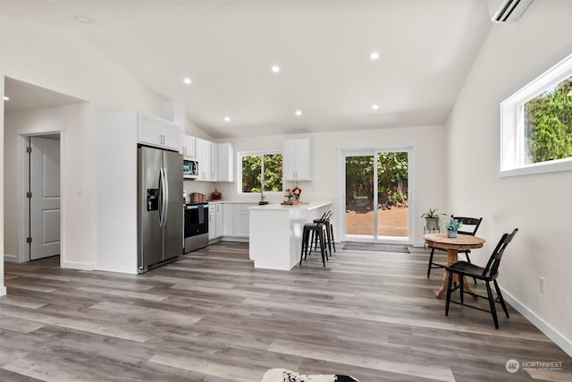 kitchen featuring lofted ceiling, a breakfast bar area, wood-type flooring, stainless steel appliances, and white cabinets