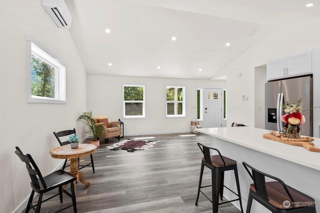 kitchen with lofted ceiling, a breakfast bar area, stainless steel fridge with ice dispenser, an AC wall unit, and white cabinets