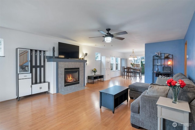 living room with a tiled fireplace, ceiling fan with notable chandelier, and hardwood / wood-style flooring