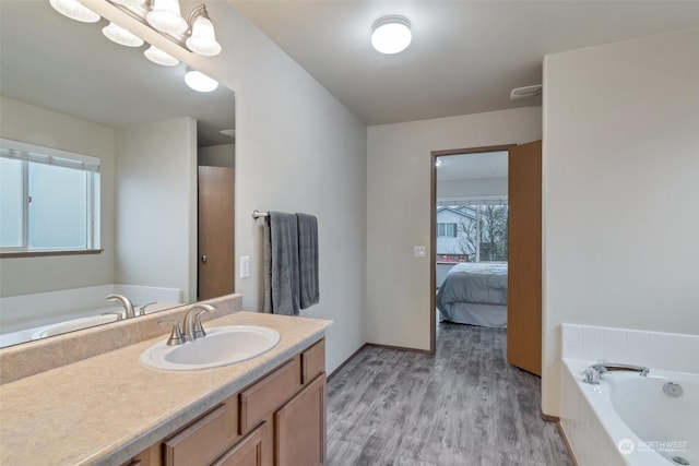 bathroom with hardwood / wood-style flooring, vanity, and tiled bath