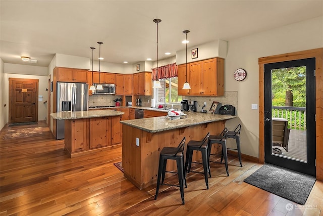 kitchen with kitchen peninsula, decorative backsplash, a healthy amount of sunlight, hanging light fixtures, and appliances with stainless steel finishes