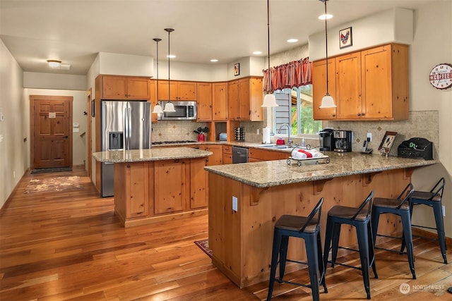 kitchen featuring hanging light fixtures, backsplash, kitchen peninsula, and appliances with stainless steel finishes