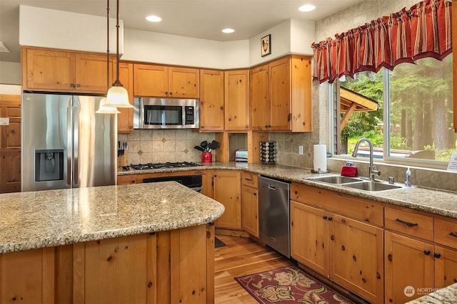 kitchen with light stone countertops, light hardwood / wood-style flooring, decorative light fixtures, appliances with stainless steel finishes, and sink