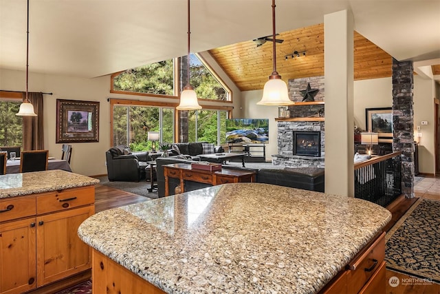 kitchen featuring light stone countertops, pendant lighting, a center island, wood ceiling, and a stone fireplace