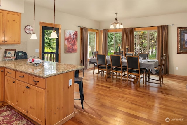 kitchen featuring a kitchen bar, decorative backsplash, light stone countertops, a chandelier, and pendant lighting