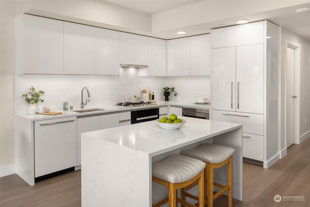1250 Alki Ave SW Unit 3B, Seattle, WA 98116 - kitchen with wall oven, a kitchen bar, wood finished floors, white cabinets, and recessed lighting