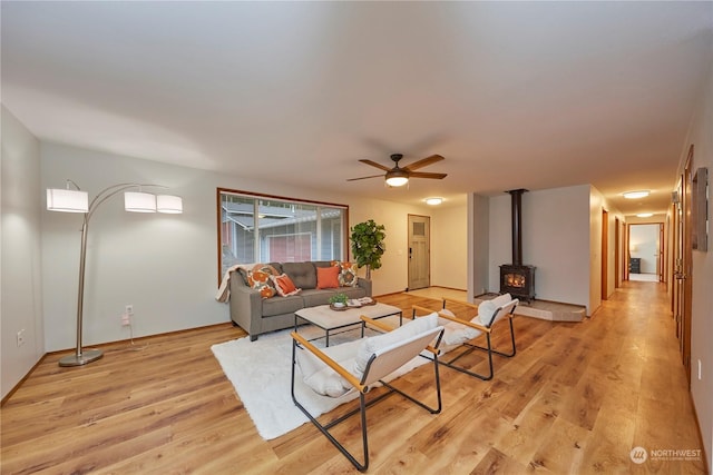 living room with light hardwood / wood-style floors, a wood stove, and ceiling fan