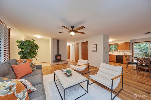 living room with ceiling fan, light wood-type flooring, a wood stove, and sink