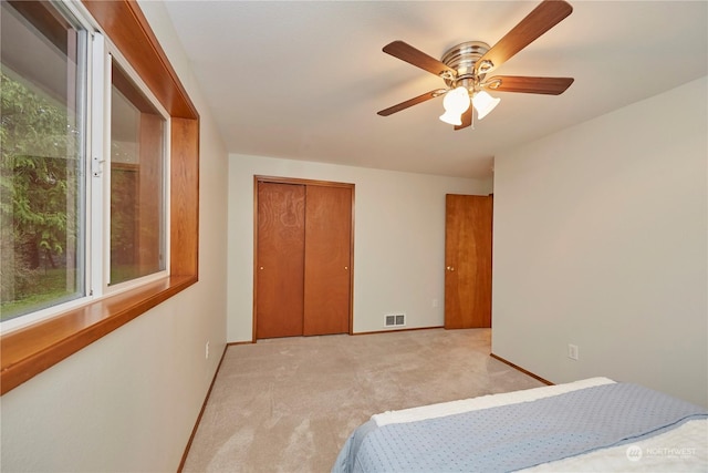 bedroom with ceiling fan, light carpet, and a closet