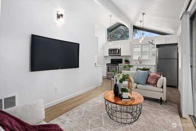 living room featuring sink, an inviting chandelier, lofted ceiling with beams, and light hardwood / wood-style floors