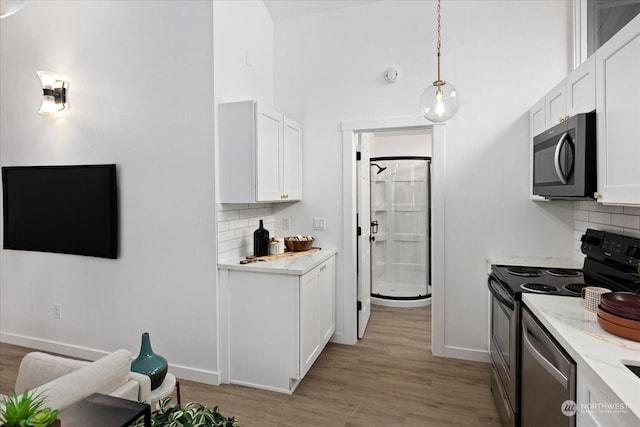 kitchen with hanging light fixtures, light stone counters, decorative backsplash, white cabinets, and appliances with stainless steel finishes