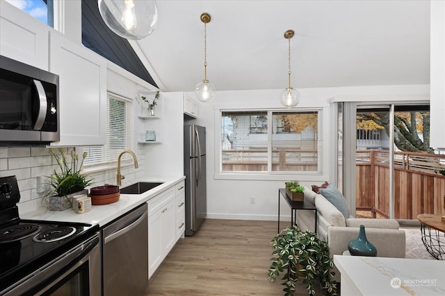 kitchen with backsplash, white cabinets, sink, hanging light fixtures, and stainless steel appliances