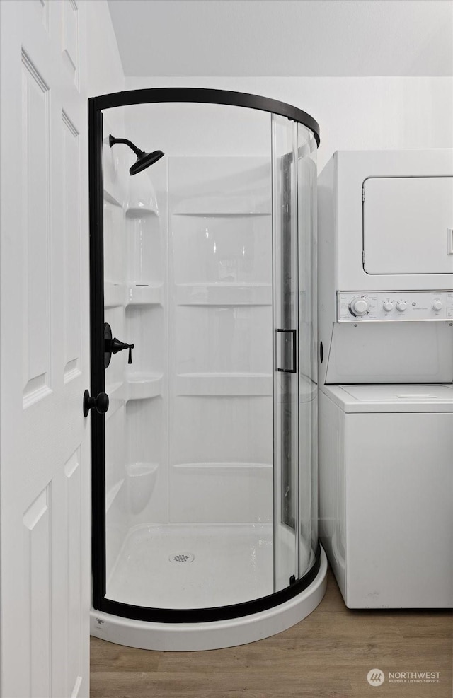 bathroom with hardwood / wood-style flooring, stacked washer / dryer, and a shower with door