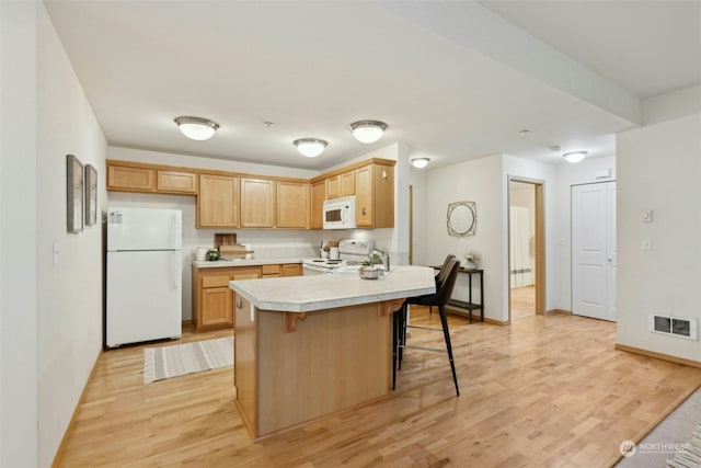 kitchen with white appliances, a breakfast bar area, light brown cabinetry, and light hardwood / wood-style flooring