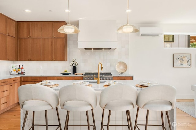 kitchen with backsplash, custom range hood, a wall unit AC, decorative light fixtures, and light hardwood / wood-style flooring