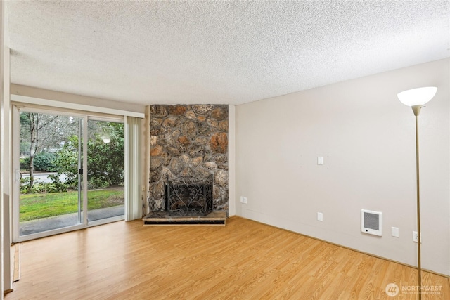 unfurnished living room featuring a stone fireplace, light hardwood / wood-style flooring, and a textured ceiling