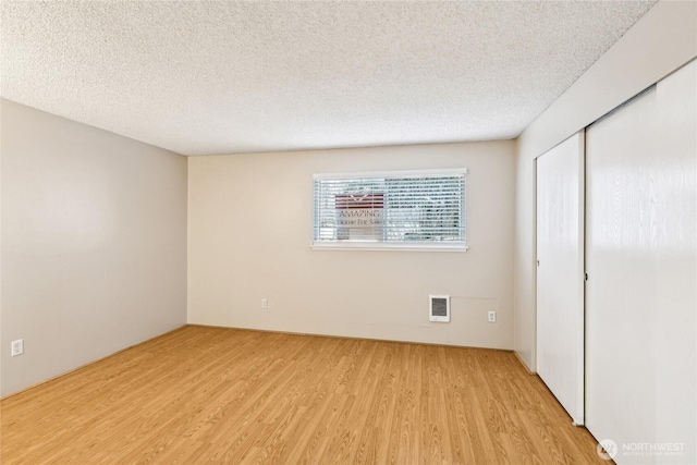 unfurnished bedroom featuring a textured ceiling, light hardwood / wood-style floors, and a closet