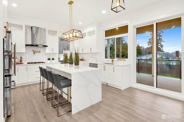 kitchen with white cabinets, sink, a kitchen island, and wall chimney range hood