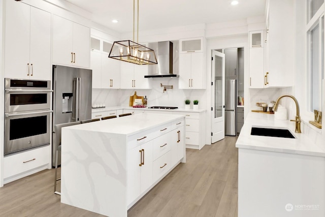 kitchen featuring appliances with stainless steel finishes, wall chimney exhaust hood, a kitchen island, sink, and white cabinetry