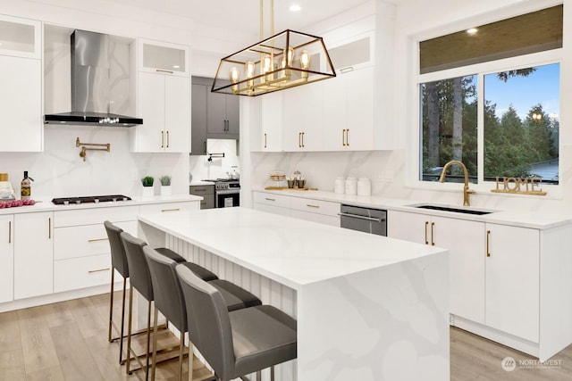 kitchen featuring white cabinets, wall chimney exhaust hood, decorative light fixtures, and a kitchen island