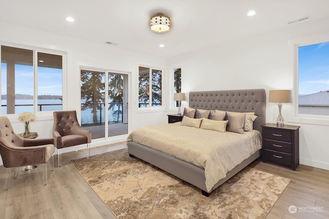 bedroom featuring light hardwood / wood-style floors, a water view, access to outside, and multiple windows