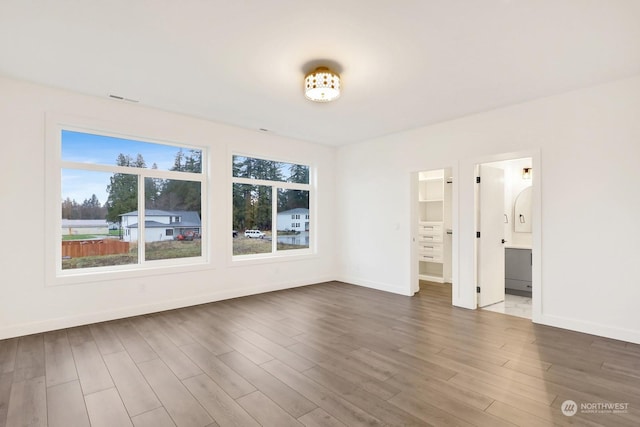 unfurnished bedroom featuring ensuite bath, a spacious closet, and dark hardwood / wood-style flooring