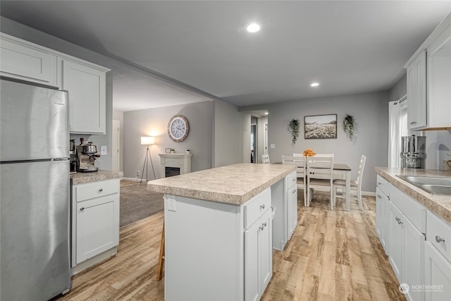 kitchen featuring white cabinets, a center island, stainless steel refrigerator, and light hardwood / wood-style flooring