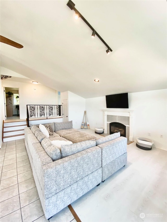 living room with rail lighting, vaulted ceiling, and a tiled fireplace