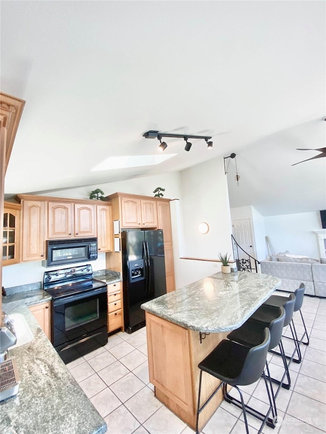 kitchen with black appliances, vaulted ceiling, light tile patterned floors, light stone counters, and a breakfast bar area