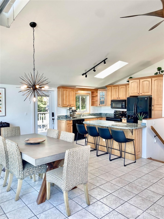 dining space with ceiling fan, vaulted ceiling with skylight, and light tile patterned floors