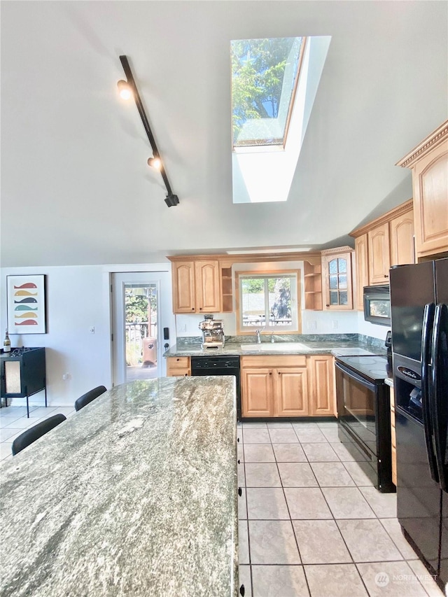 kitchen featuring light stone countertops, track lighting, vaulted ceiling with skylight, black appliances, and light tile patterned flooring