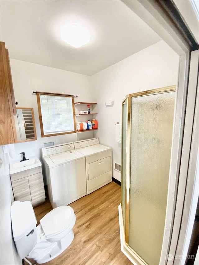 bathroom featuring separate washer and dryer, an enclosed shower, toilet, vanity, and hardwood / wood-style flooring