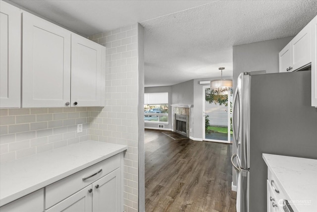 kitchen with dark wood-type flooring, stainless steel refrigerator, pendant lighting, decorative backsplash, and white cabinets