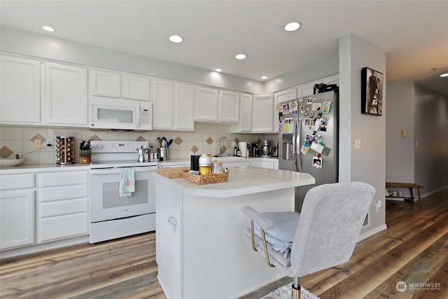 kitchen with white appliances, hardwood / wood-style flooring, a center island, decorative backsplash, and white cabinets