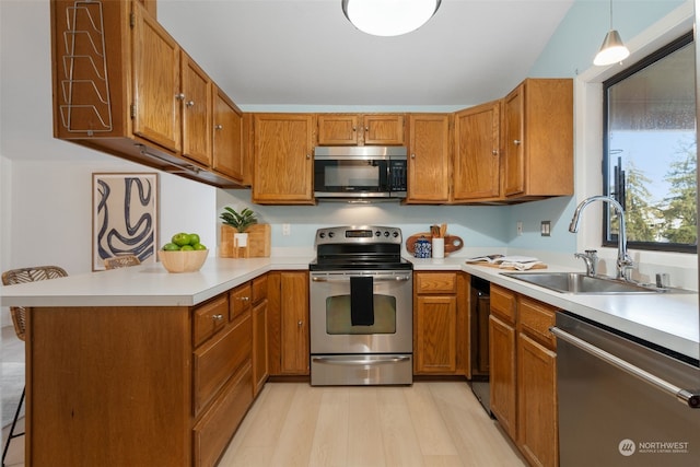 kitchen with sink, kitchen peninsula, pendant lighting, appliances with stainless steel finishes, and light wood-type flooring