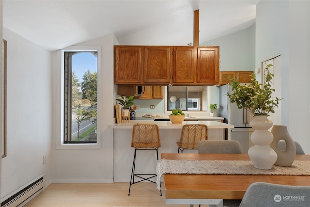 kitchen featuring baseboard heating, light hardwood / wood-style flooring, a kitchen bar, and lofted ceiling