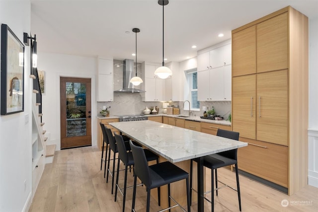 kitchen featuring decorative light fixtures, white cabinetry, wall chimney range hood, and backsplash