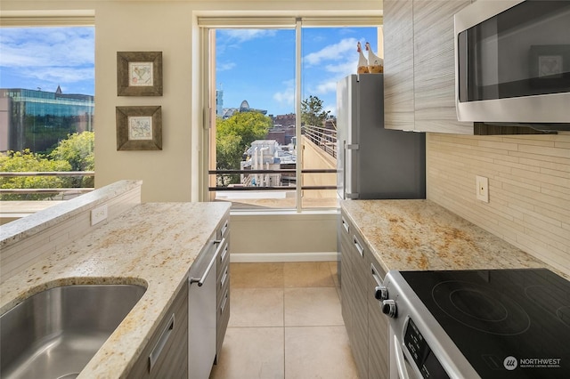 kitchen with sink, decorative backsplash, light stone countertops, light tile patterned flooring, and stainless steel appliances