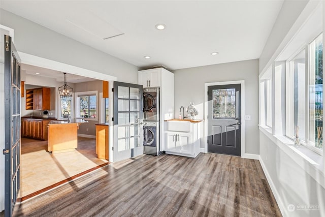 kitchen with stacked washing maching and dryer, kitchen peninsula, decorative light fixtures, white cabinets, and light wood-type flooring