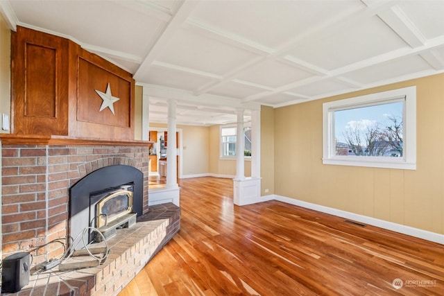 living room with beam ceiling, a wood stove, coffered ceiling, decorative columns, and light wood-type flooring