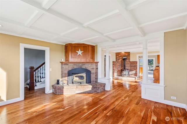 unfurnished living room with beam ceiling, a wood stove, coffered ceiling, decorative columns, and hardwood / wood-style flooring