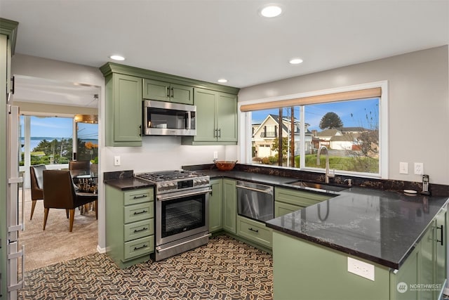 kitchen featuring kitchen peninsula, green cabinets, stainless steel appliances, dark stone countertops, and sink