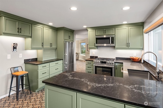 kitchen featuring stainless steel appliances, green cabinetry, sink, kitchen peninsula, and dark stone counters