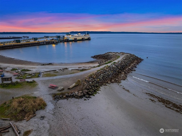 aerial view at dusk featuring a water view and a view of the beach