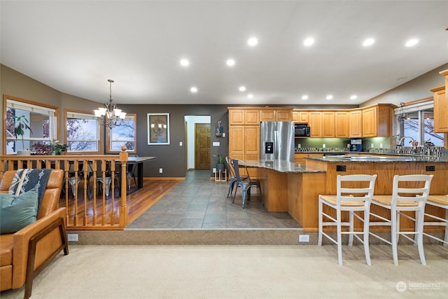 kitchen with dark stone counters, a kitchen breakfast bar, decorative light fixtures, a notable chandelier, and stainless steel fridge with ice dispenser